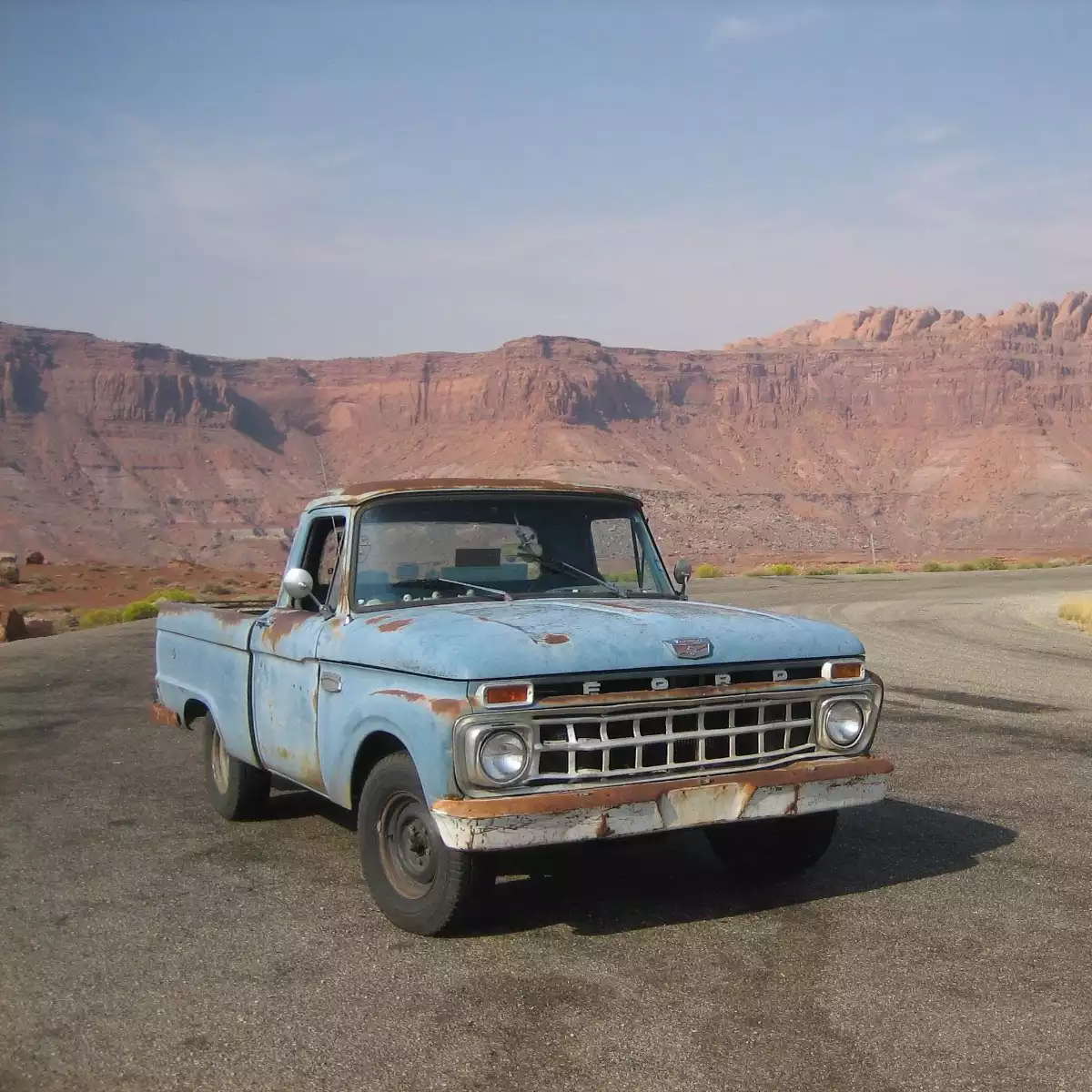 Oblique view of a parked vintage blue truck with desert mountains in the background.